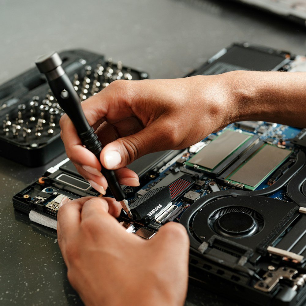 Technician using a screwdriver to repair an open laptop motherboard